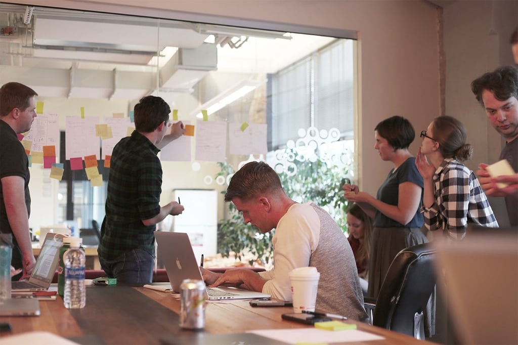 Group of six people collaborating using sticky notes on a window.