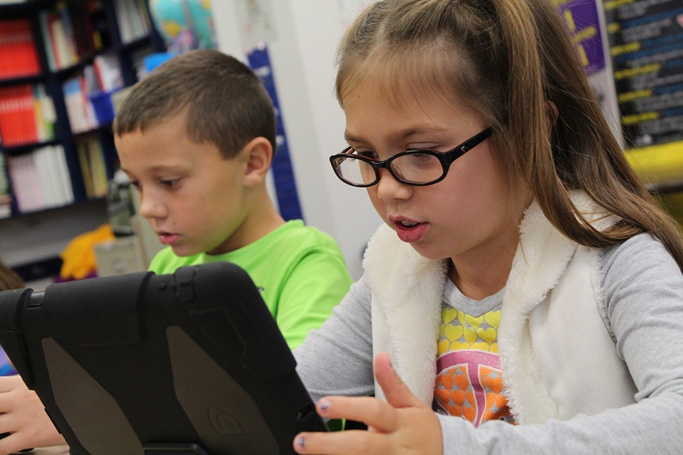 Two children in a classroom looking at a tablet devices.