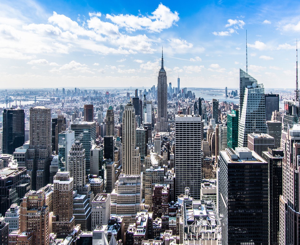 High level view of city buildings under a blue sky with white clouds.