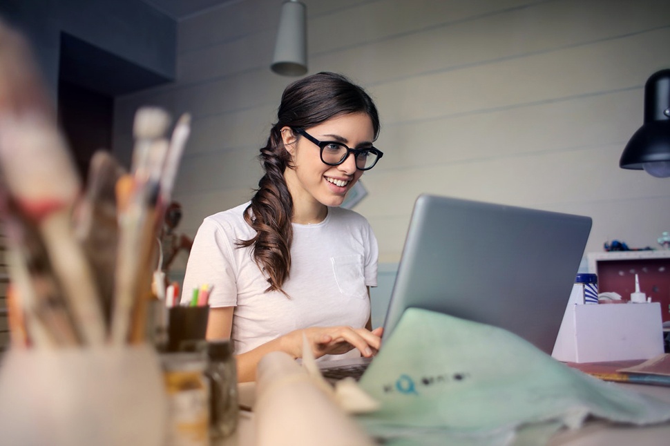 Woman typing on a laptop surrounded by art materials.