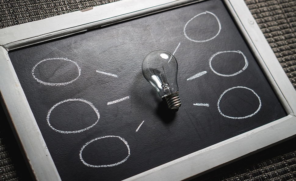Light bulb on a small blackboard surrounded by idea circles drawn in chalk.
