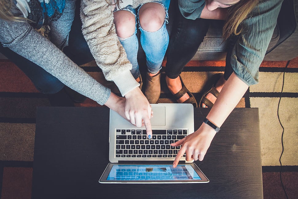 Three people sitting around and pointing at a laptop computer.