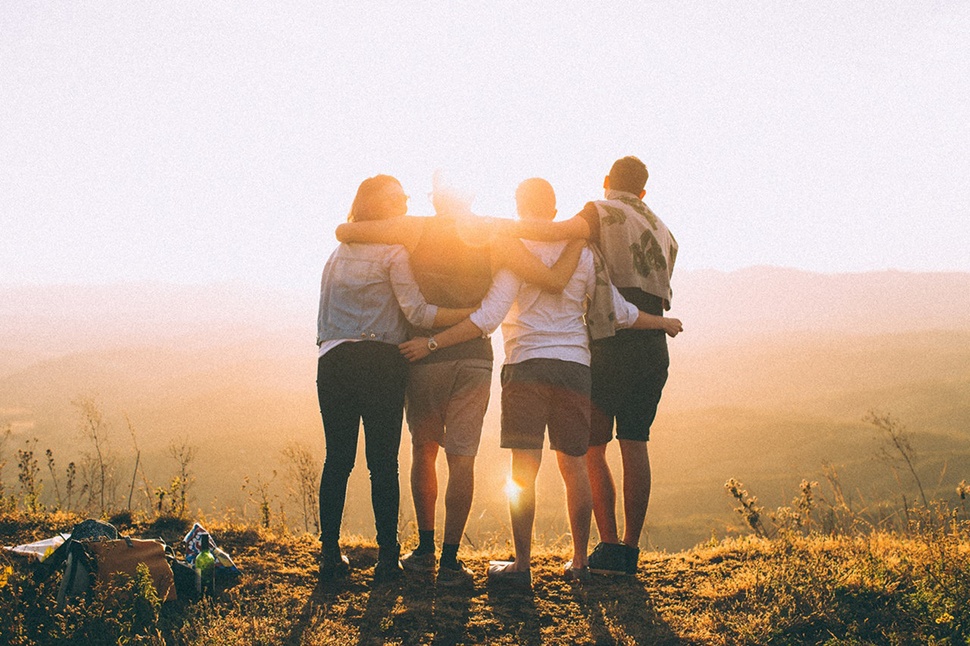 Four people with their backs to the camera overlooking a hillside on a bright day.