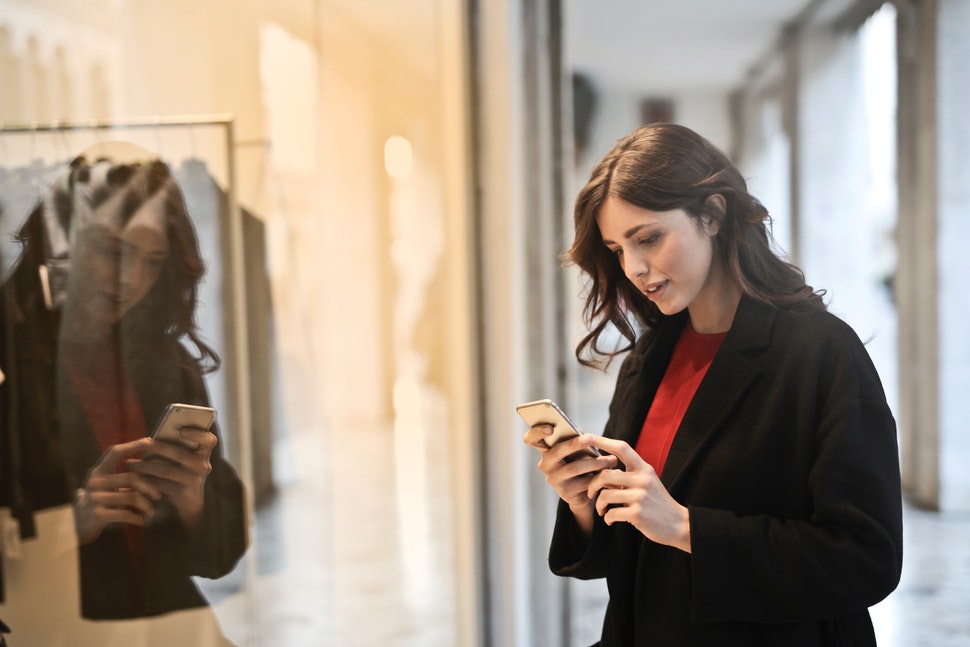 A woman standing in front of a store window, looking at her mobile device