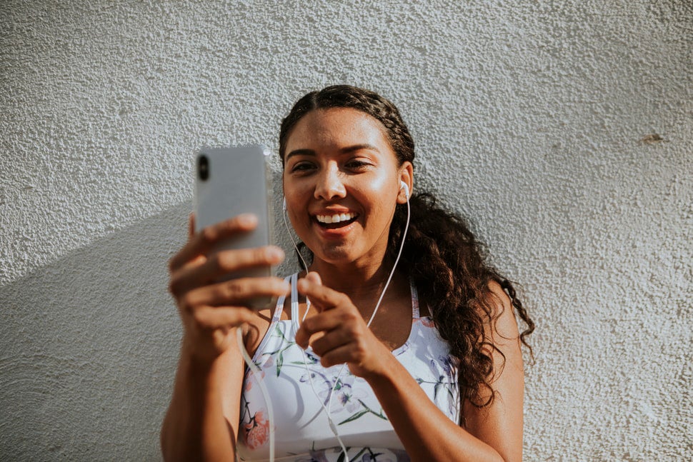 Woman wearing fitness outfit and ear buds, smiling while using her smartphone