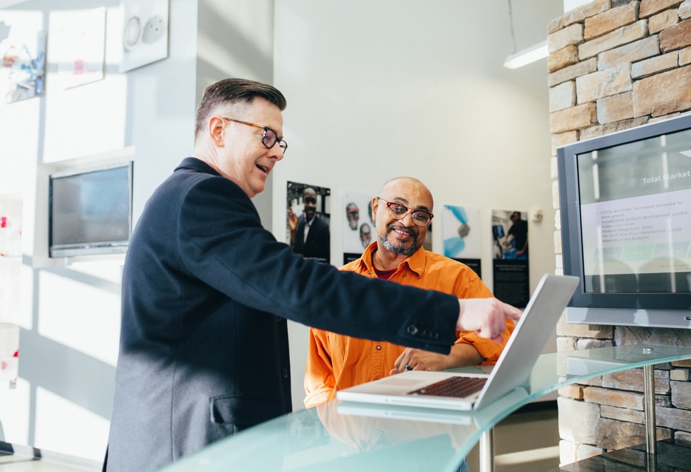 Two smiling men looking at a laptop, one of them pointing at the screen