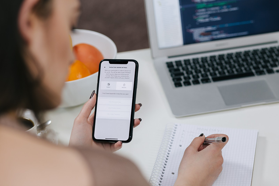 Woman holding a smartphone and writing on a note pad.