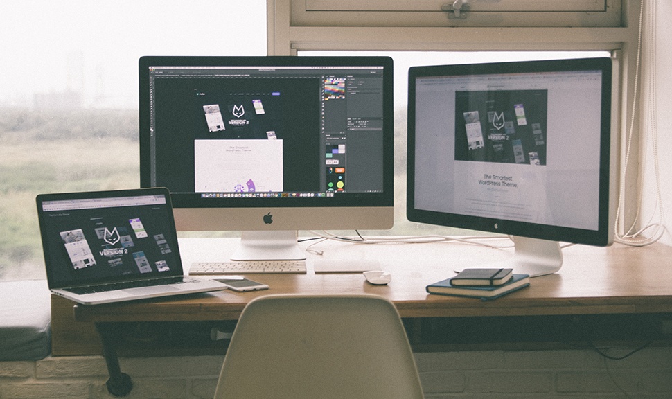 Two apple computer monitors and a laptop on a desk with web hosting graphics