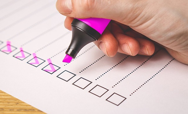 A hand holding a pink highlighter over a piece of paper with pink check marks in some of the checkboxes.