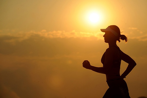 Woman in exercise clothes running with bright sunlight in the background.